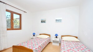 Una stanza con due letti singoli, ognuno con un comodino e una lampada. Si vede una finestra con tende e due quadri appesi al muro.