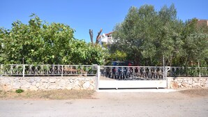 A gated property with a stone wall and metal fence, surrounded by trees and a clear blue sky. - Apartments Goroslava (Tribunj)