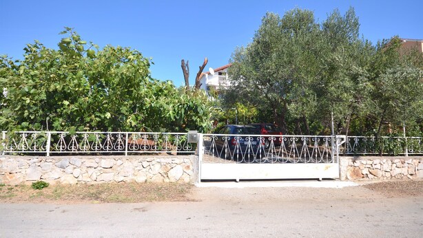 Una proprietà recintata con un muro in pietra e un cancello in metallo, immersa tra alberi e un cielo azzurro intenso.