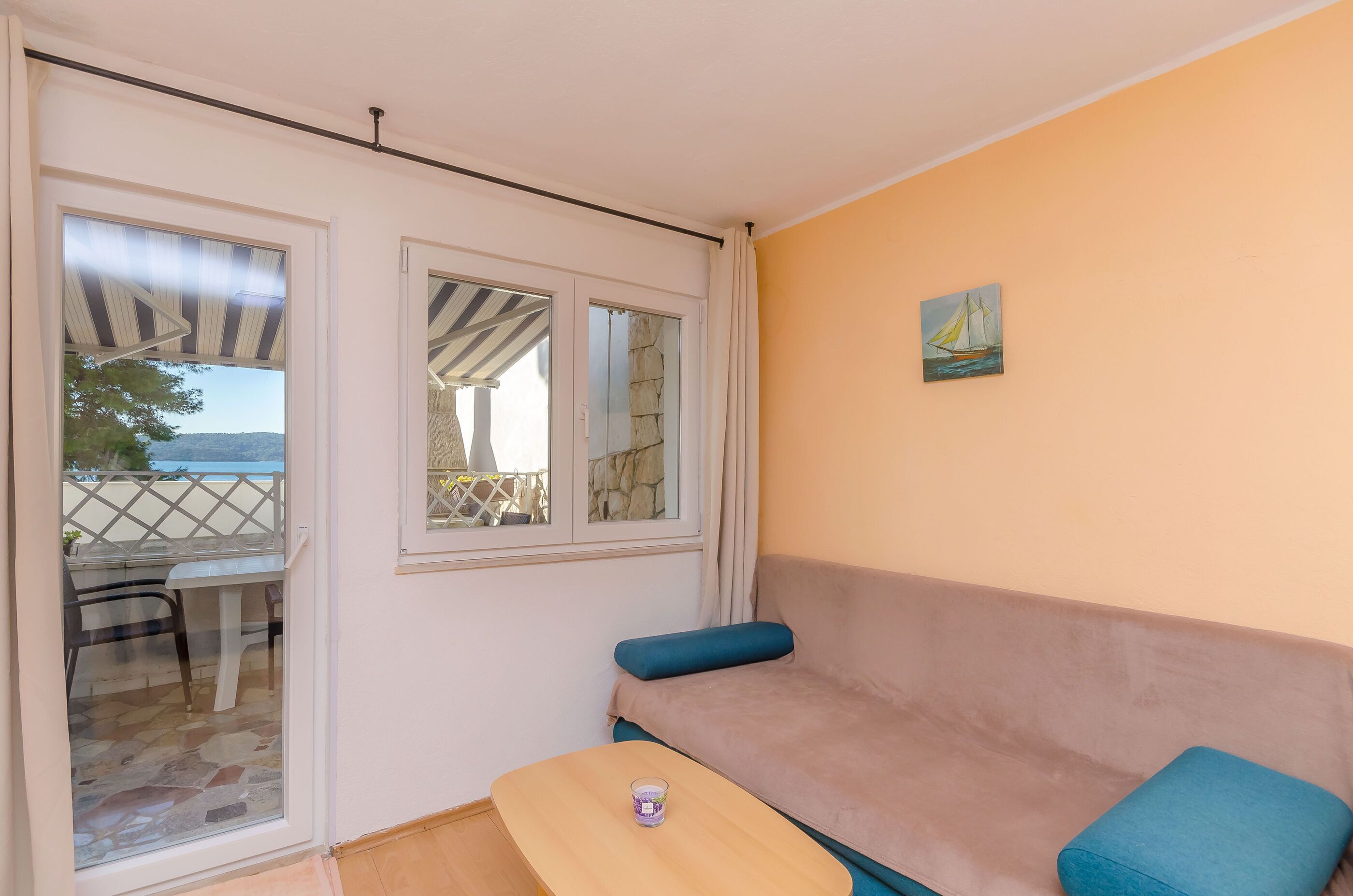 Ein Zimmer mit einem beigen Sofa, einem kleinen Tisch und Blick auf einen Balkon mit Tisch und Stühlen.