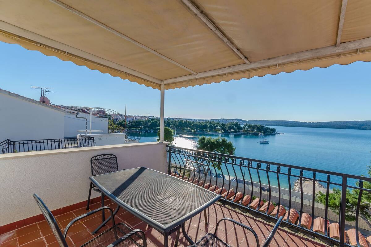 A balcony with a table and chairs, overlooking a lake with boats and a distant shoreline.