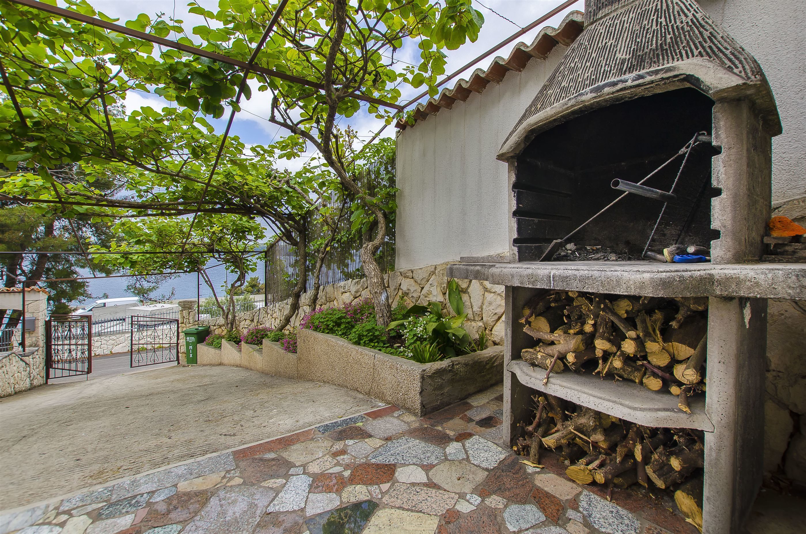 Eine Terrasse im Freien mit Steinplattenboden, einem Grill und einer Steinmauer.