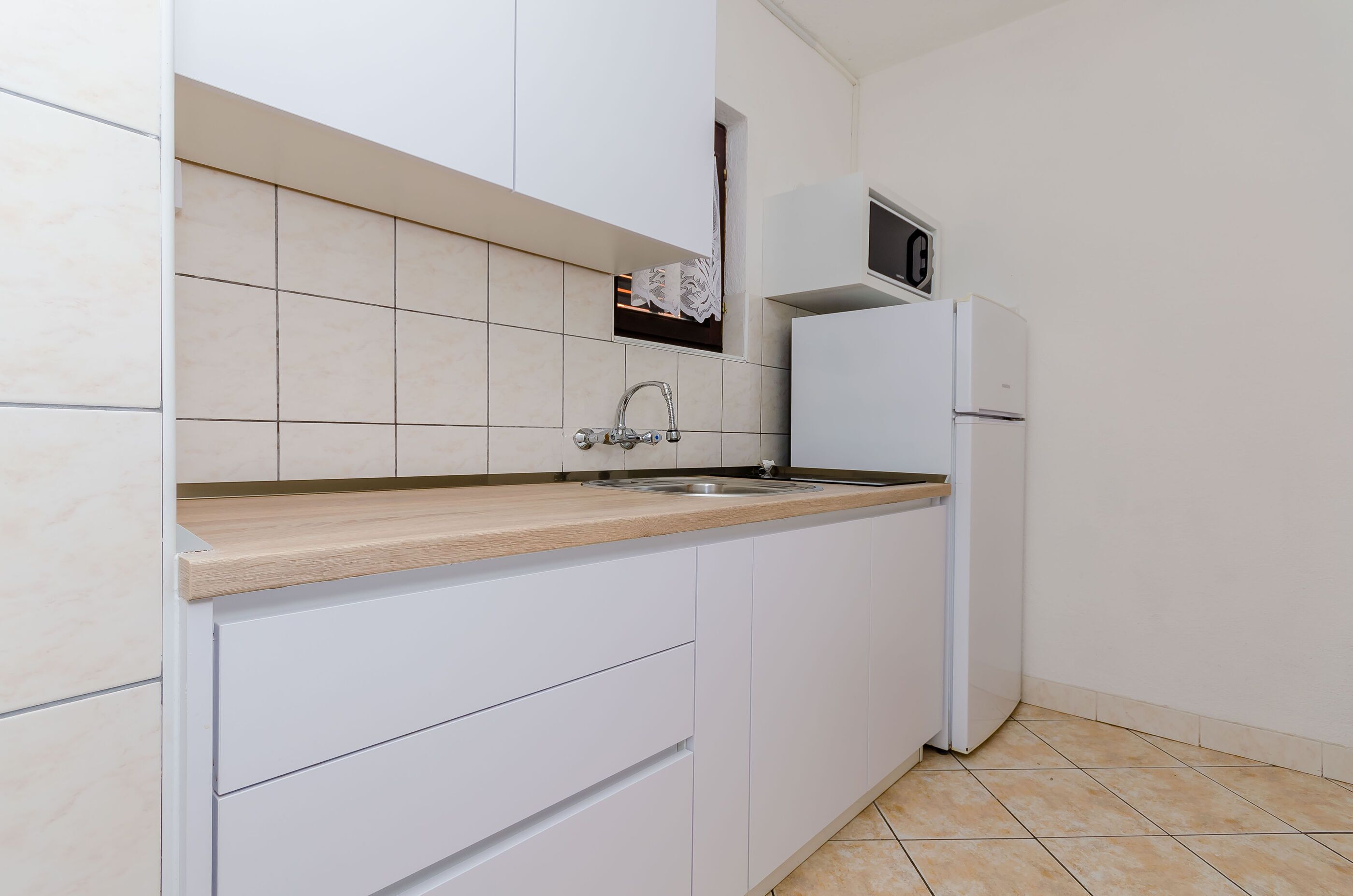 A kitchen with white cabinets, a wooden countertop, a stainless steel sink, and a white refrigerator.