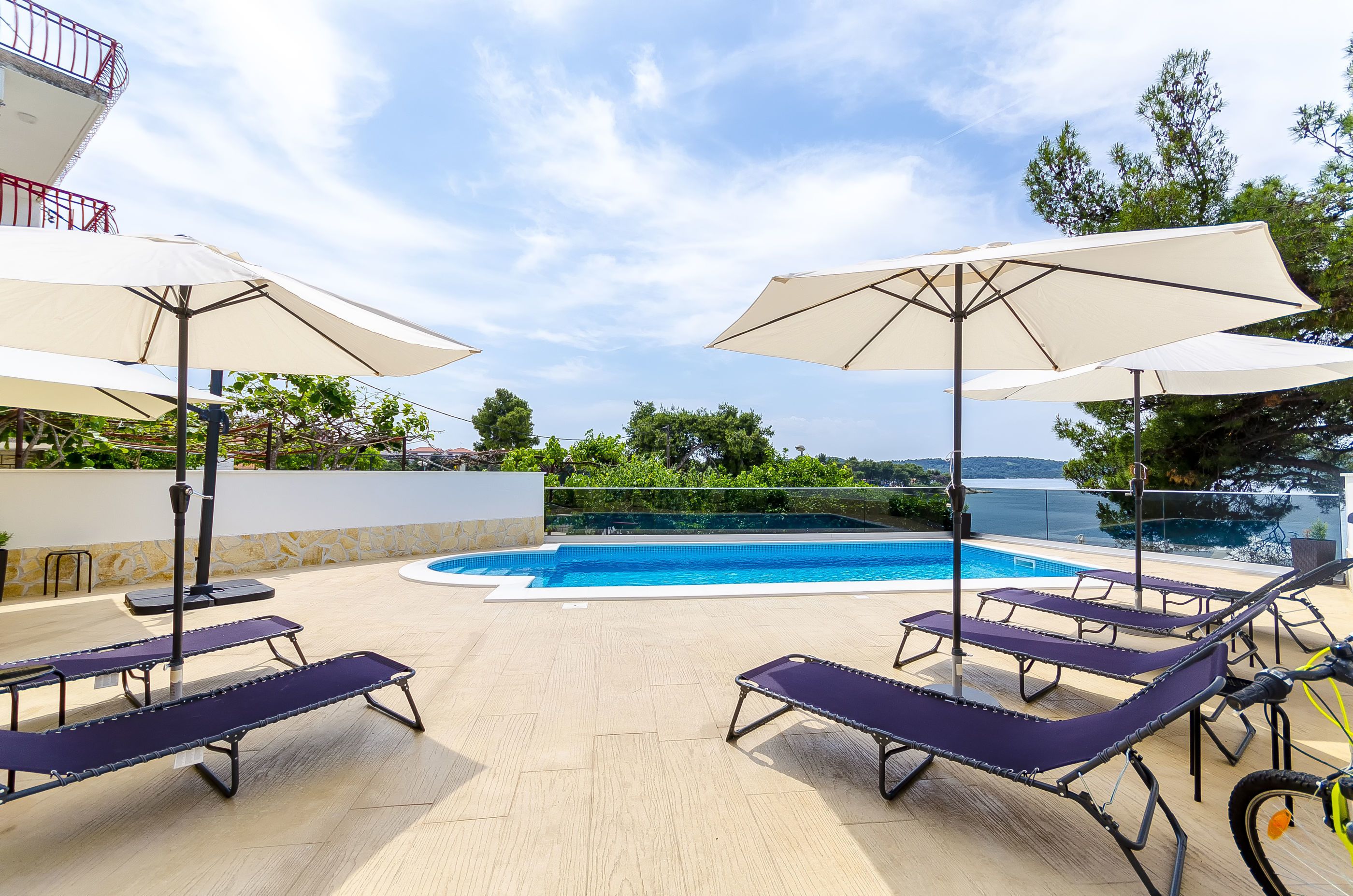 A rooftop pool area with lounge chairs and umbrellas, overlooking a clear blue pool and distant landscape.