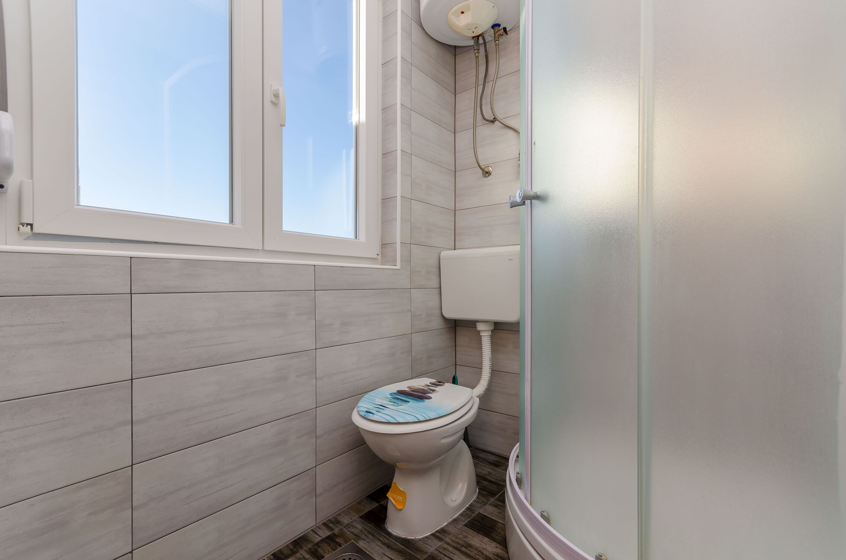 A bathroom with a toilet, a window, and a shower area.