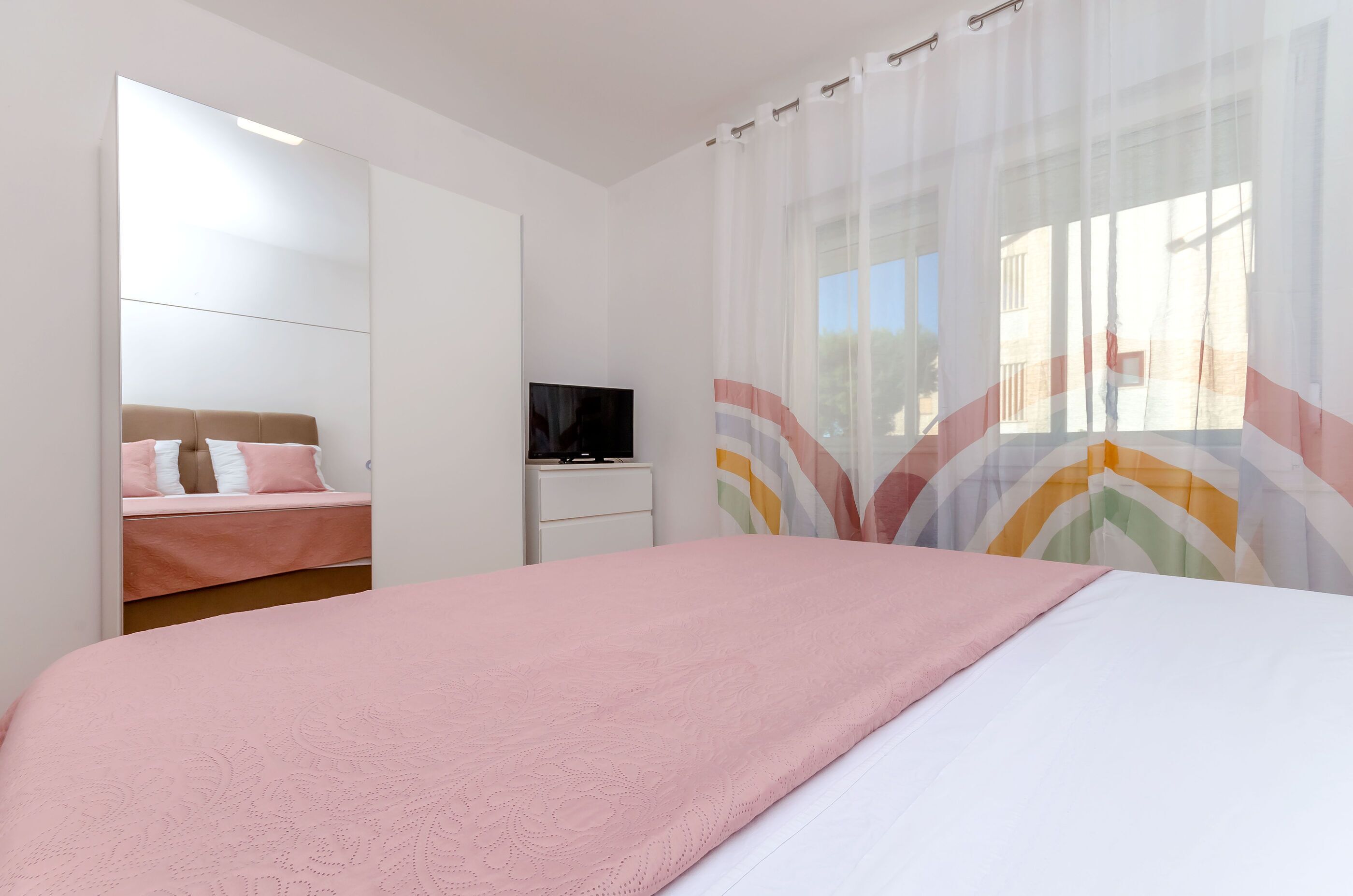 Un dormitorio con cama, televisión, armario y ventana con cortinas.