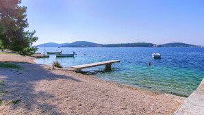 Ein Kiesstrand mit einer hölzernen Bank und mehreren Booten auf ruhigem Wasser.