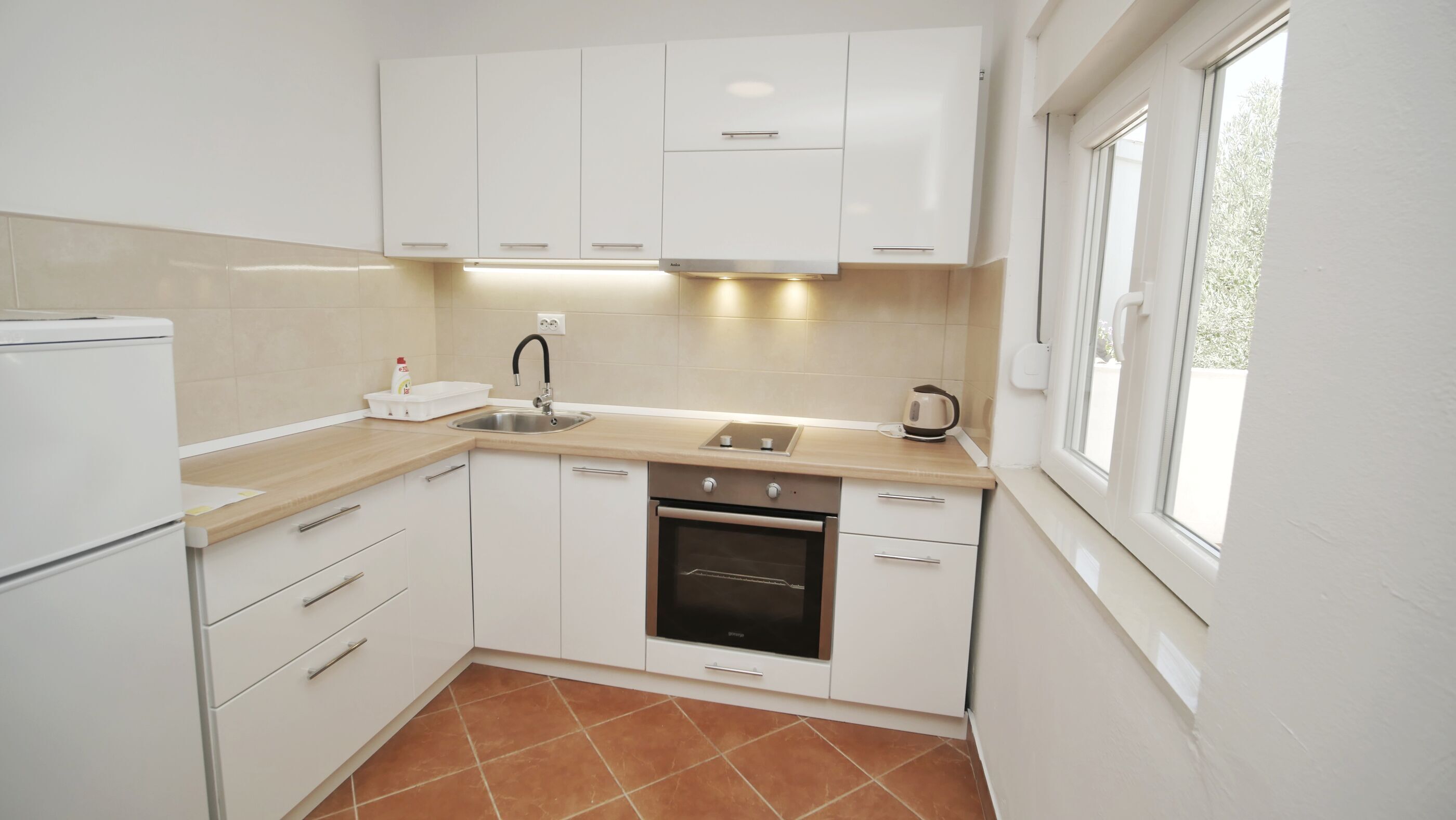 A modern kitchen with white cabinets, a built-in oven, a sink, and a window providing natural light.
