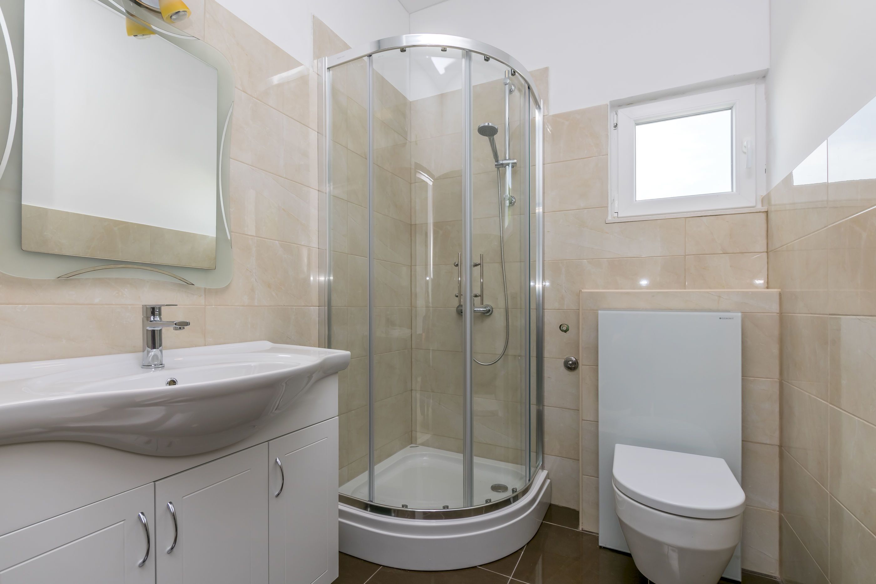 Een moderne badkamer met een douchecabine van glas, een witte wastafel en een toilet.