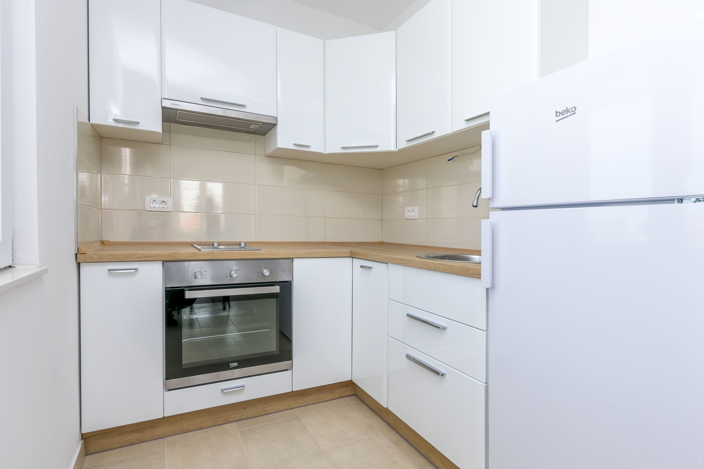A compact kitchen with white cabinets, a built-in oven, and a refrigerator.