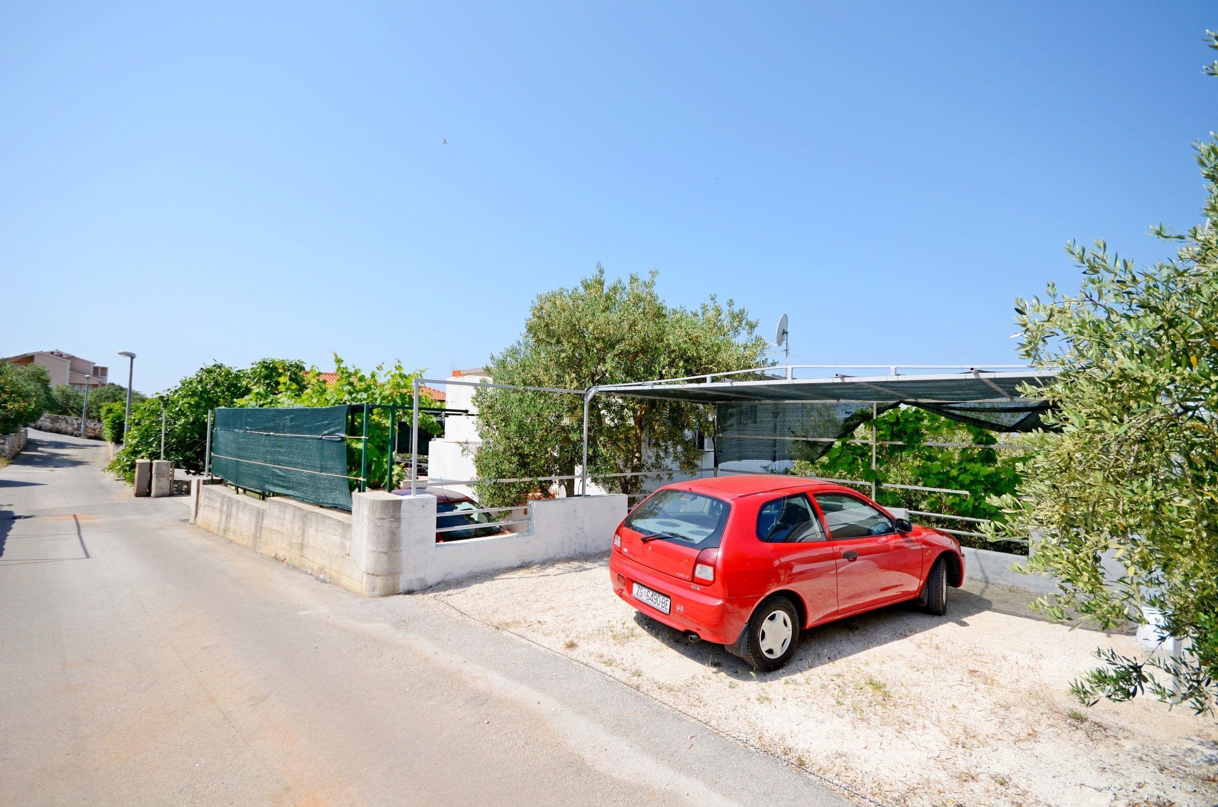 Um carro vermelho estacionado em um caminho de cascalho ao lado de um prédio com área externa coberta.