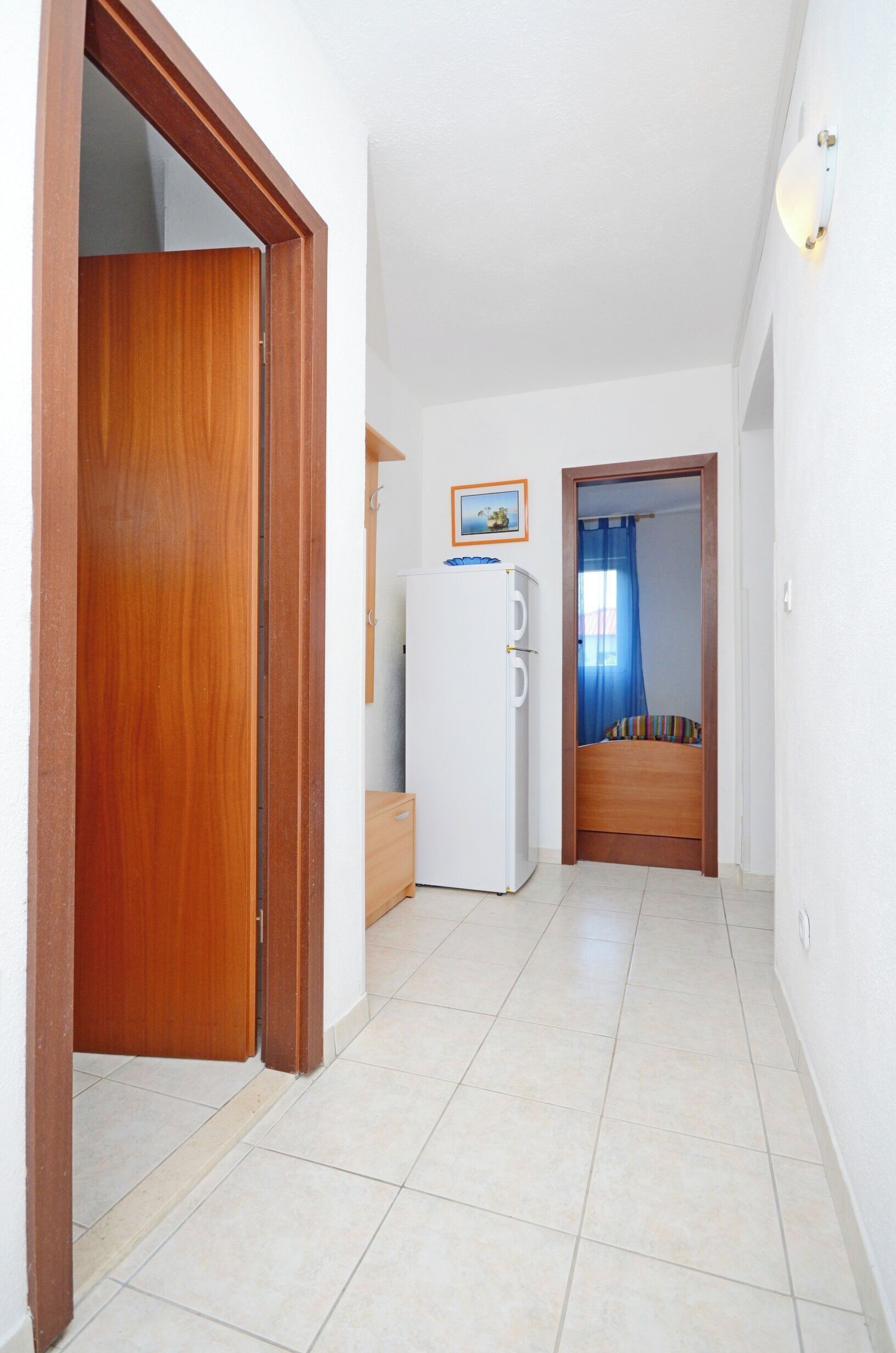 A hallway with a wooden door, a white refrigerator, and a bed with a blue curtain.