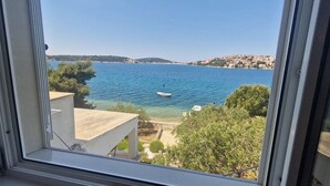 Blick auf eine Küstenlandschaft mit einem Boot auf dem Wasser, Gebäuden im Hintergrund und einem Fensterrahmen im Vordergrund.