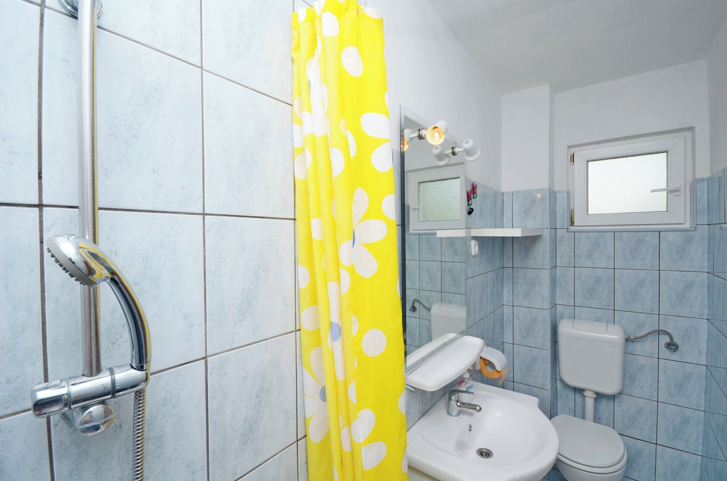 Een badkamer met douche, toilet, wastafel en een raam.