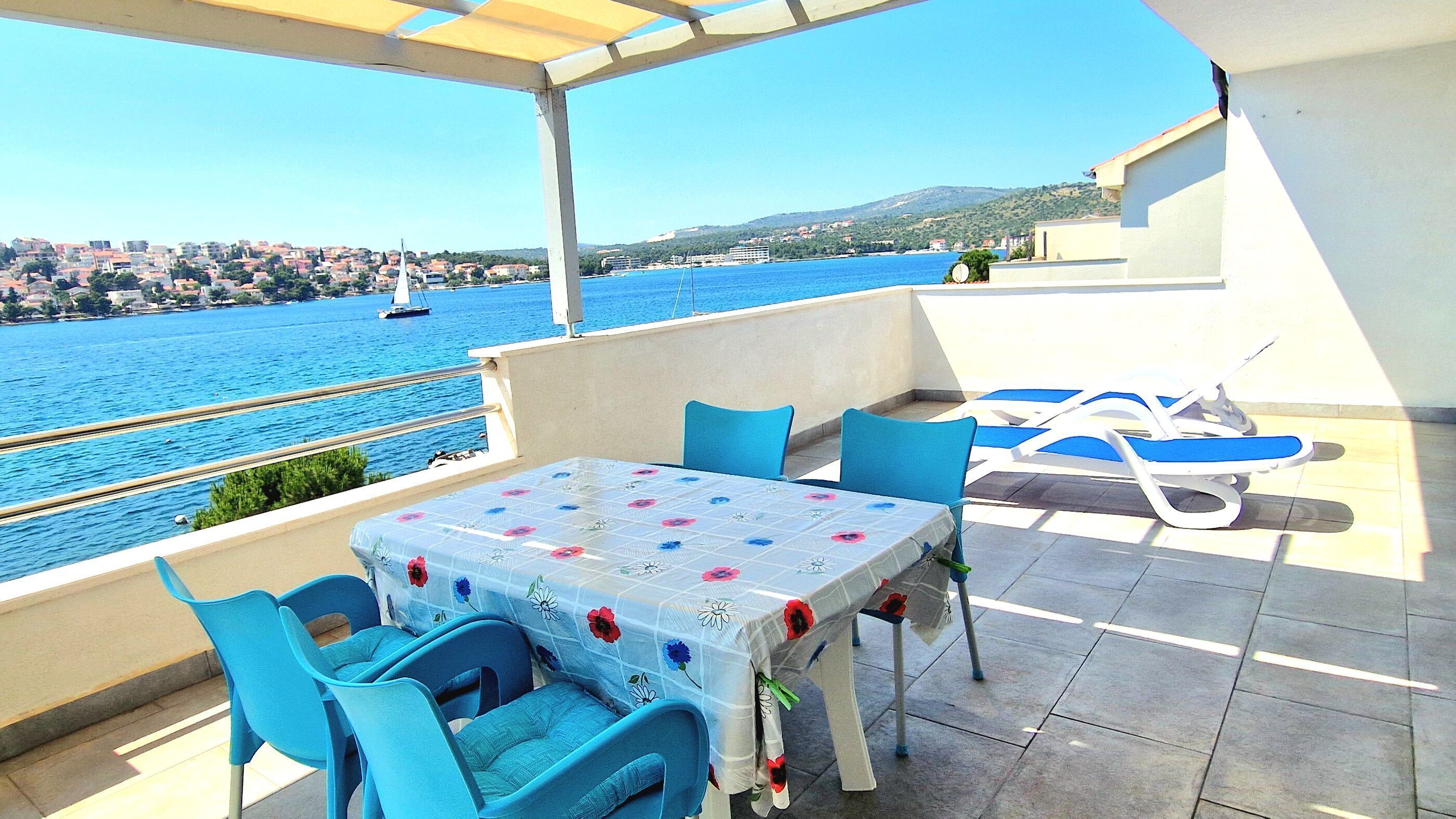 A terrace with a table and chairs, a pool area, and a view of the sea and town.
