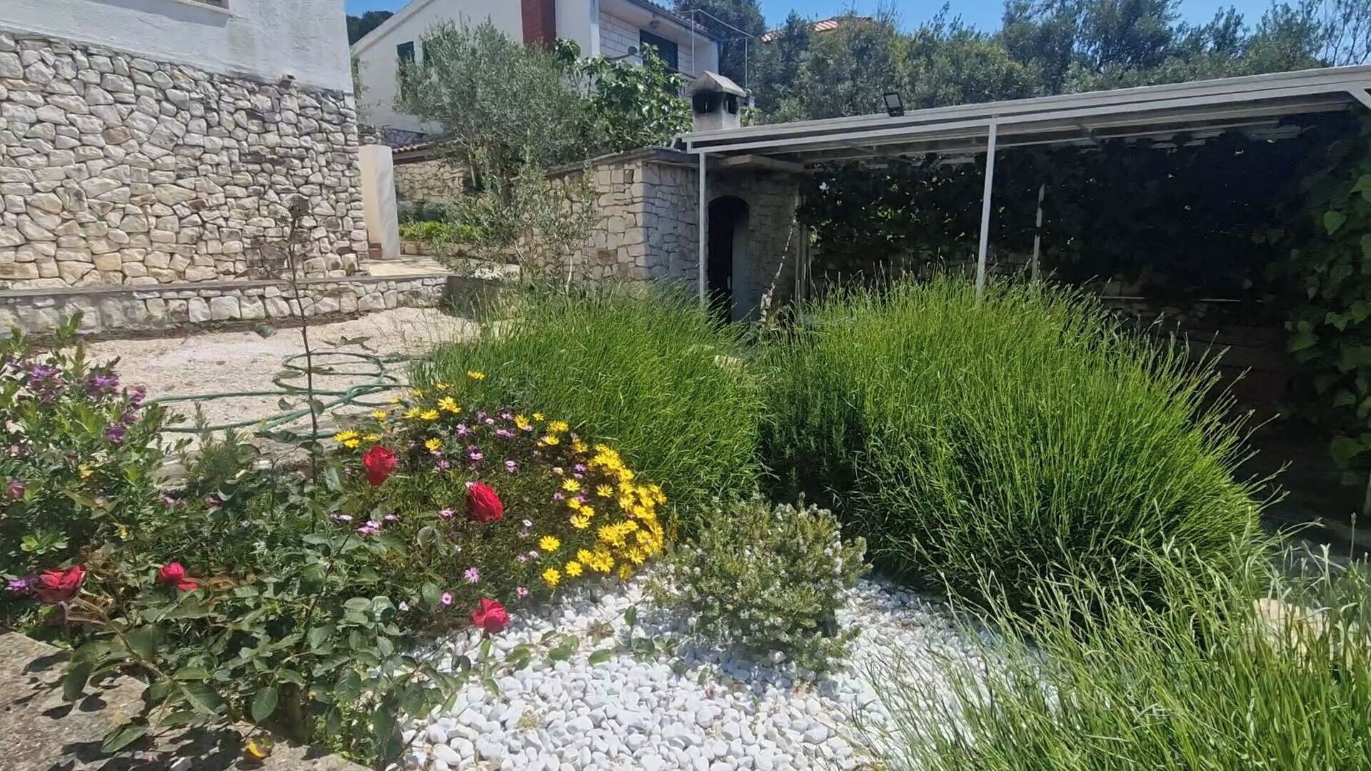 Un jardin agrémenté d’un mur en pierre, d’une pergola et de diverses plantes et fleurs.