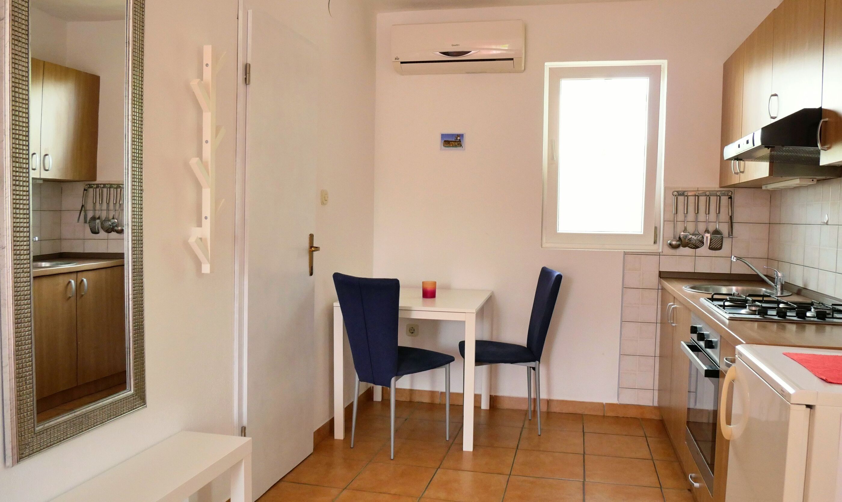 A compact kitchen with a gas stove, a small table with two chairs, and a window.