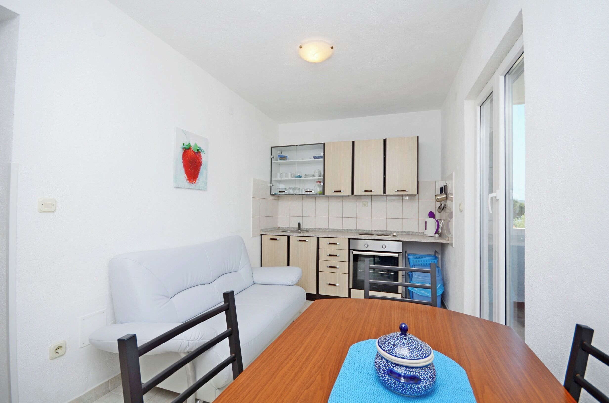 A compact kitchen with white cabinets, a dining table, and a sofa.