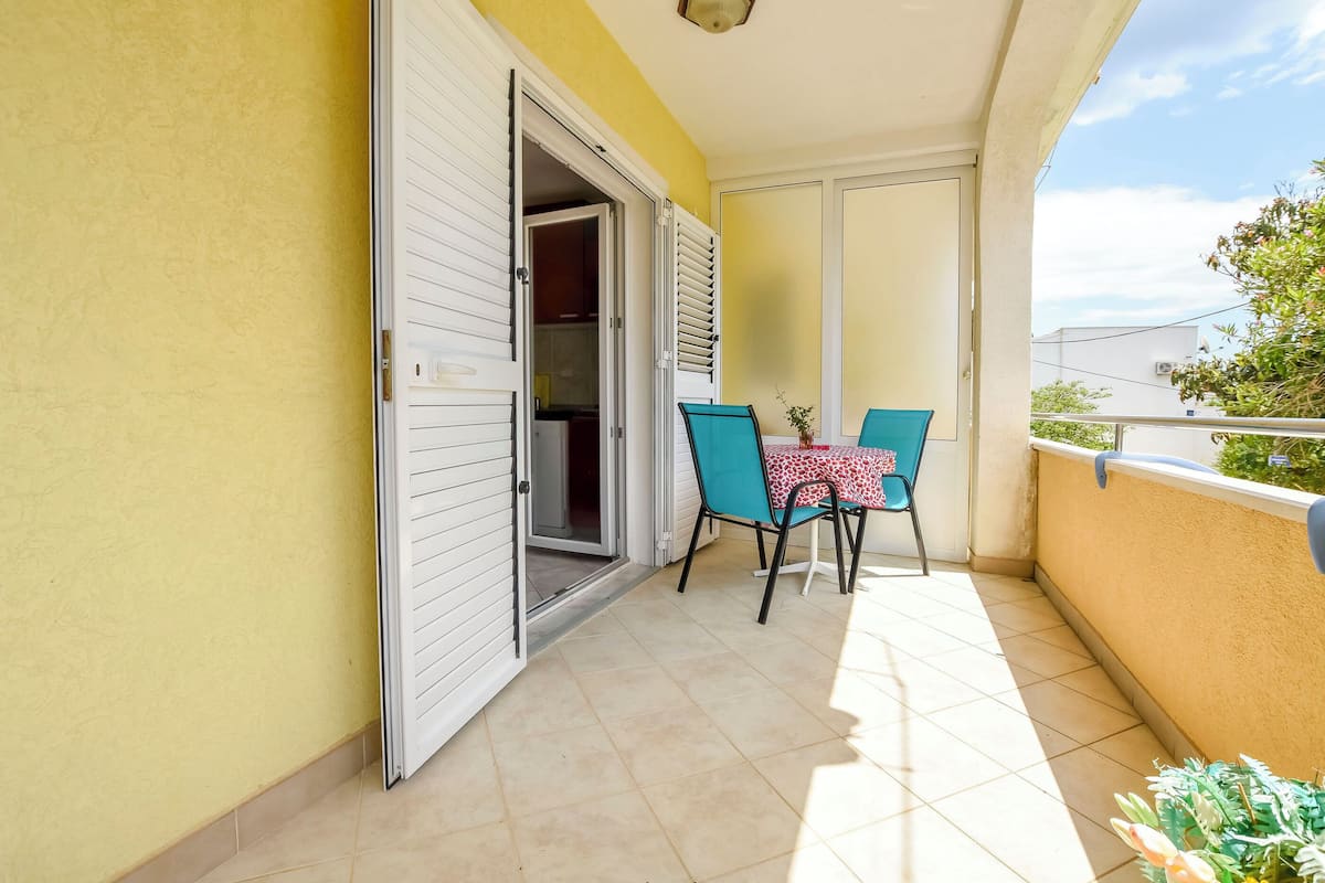 Un balcone con tavolo e sedie, una porta scorrevole e vista sul cielo.