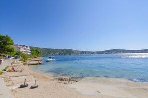 A coastal beach with clear blue water, a sandy shore, and a few boats. - Apartments Kata (Rogoznica)