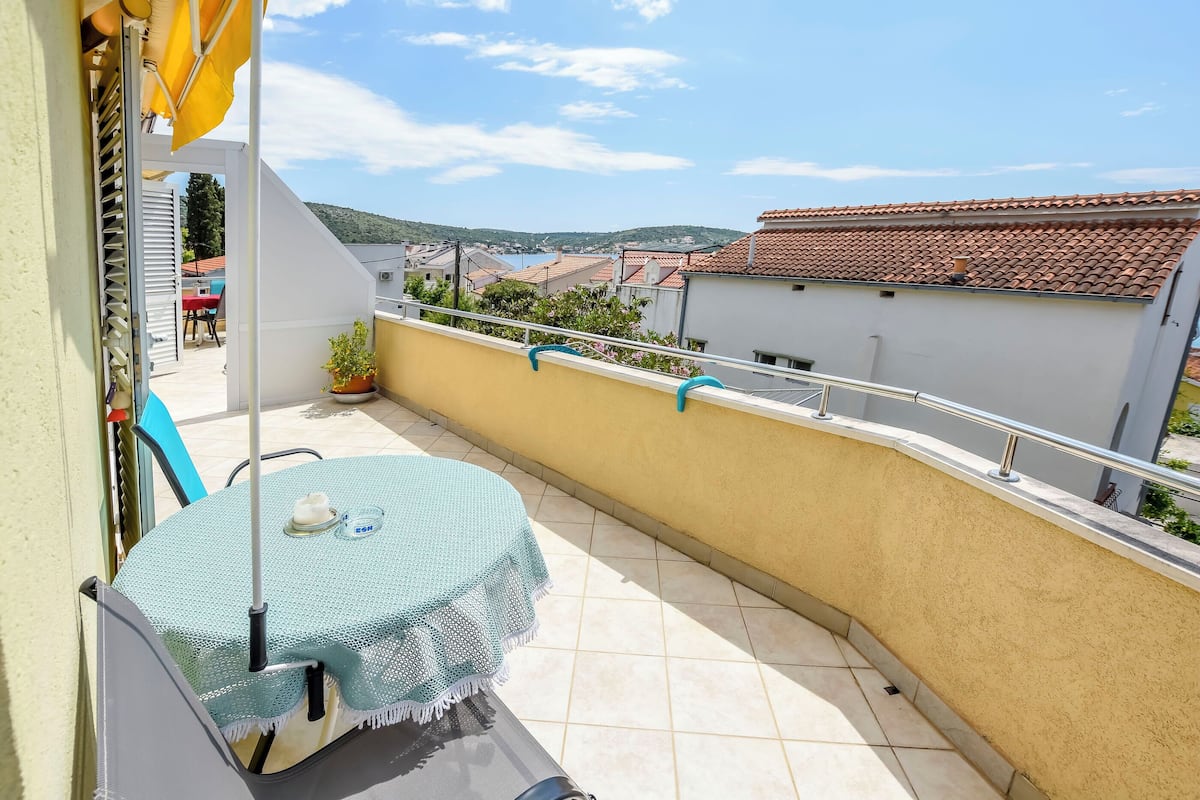 Un balcone con tavolo e sedie, un vaso di fiori e vista sul paese e le colline sullo sfondo.