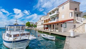 Un port de plaisance avec des bateaux amarrés, un bâtiment en pierre doté de balcons et un ciel bleu azur.