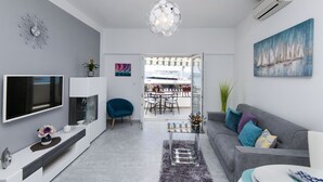 Un salon moderne doté d’un téléviseur à écran plat, d’un canapé gris et d’un coin repas avec une table et des chaises en verre.