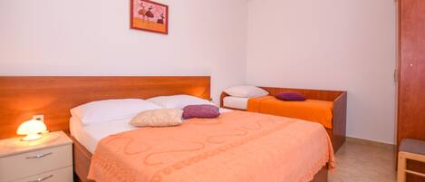 A bedroom with a wooden headboard, a bed with an orange blanket, a nightstand with a lamp, and a small table with a chair.