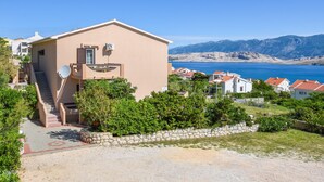 Ein hellbeige Gebäude mit Satellitenschüssel, einer Treppe und Blick auf das Meer und die Berge.