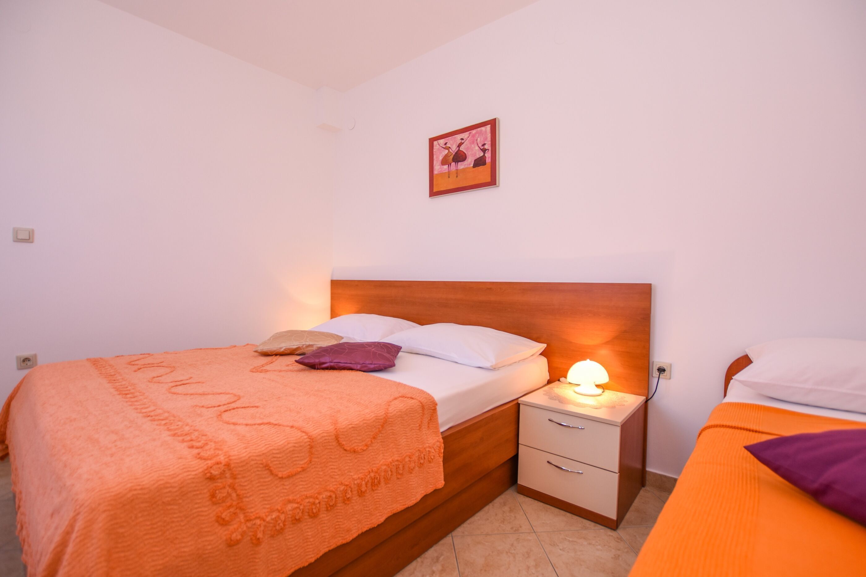 Een slaapkamer met een houten hoofdbord, een nachtkastje met een lamp, en een bed met een oranje deken.