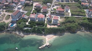 Luftaufnahme einer Küstenwohngegend mit Gebäuden, einem Strand und klarem türkisblauem Wasser.