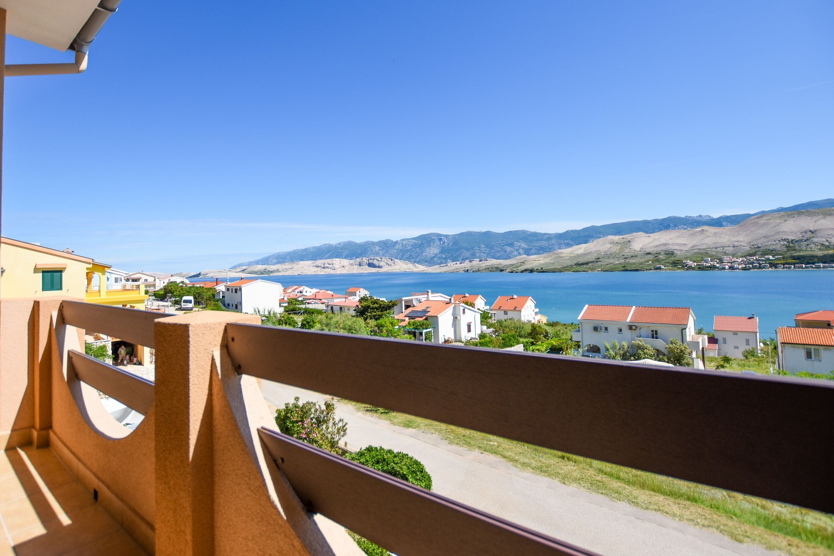 A balcony overlooking a coastal town with houses and a clear blue sky.