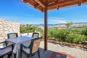 Un patio al aire libre con mesa y sillas, pared de piedra y vistas a montañas y agua.