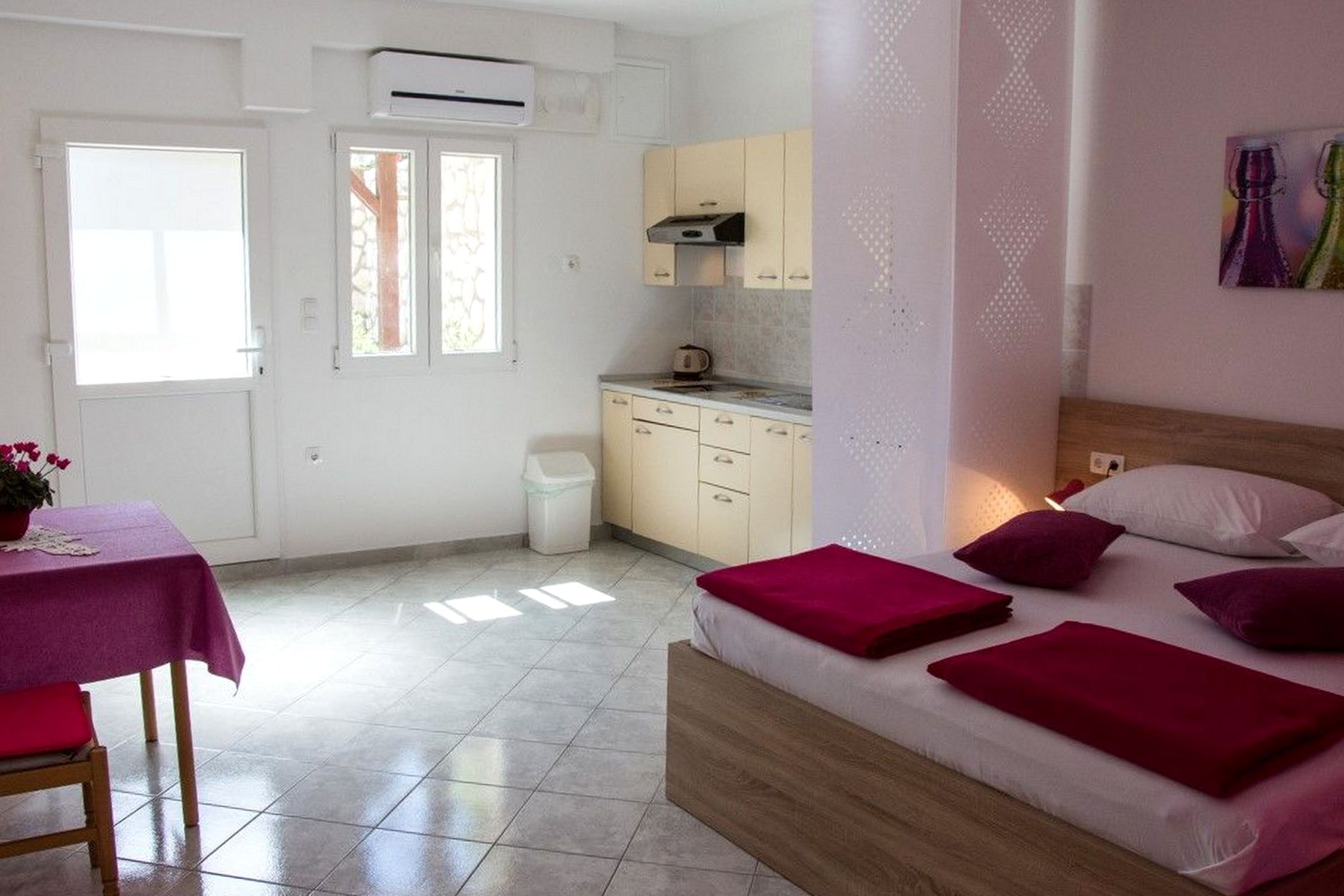 A compact hotel room with a bed, a small kitchenette, a dining table, and a window.