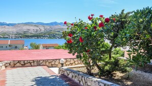 Eine Steinsäule mit rotem Dach, ein Garten mit roten Blumen und ein Blick auf einen See und Berge im Hintergrund.