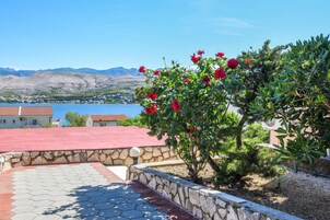 Un muro in pietra con tetto rosso, un giardino con fiori rossi e, sullo sfondo, vista su un lago e montagne.