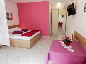 Un dormitorio con una cama, una mesa con una planta y un televisor en la pared.