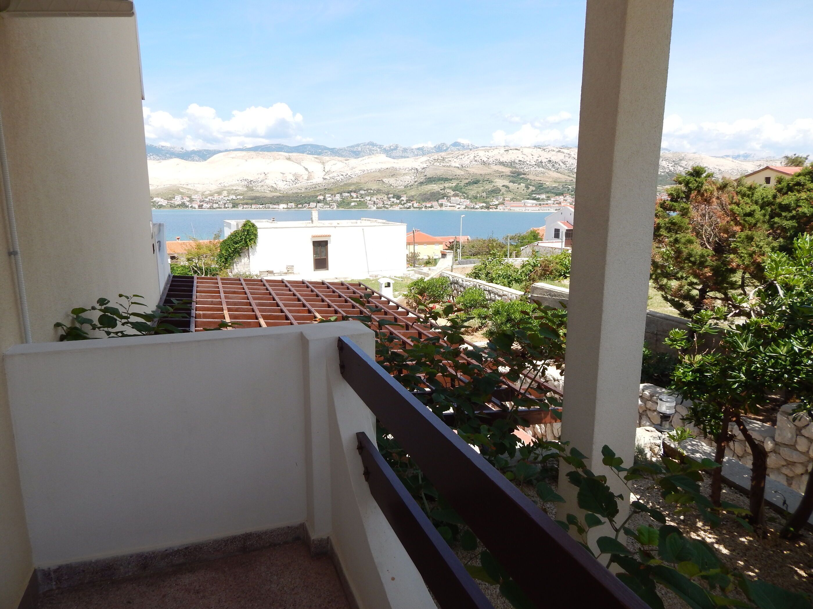 A balcony with a view of a coastal town, a body of water, and distant mountains.