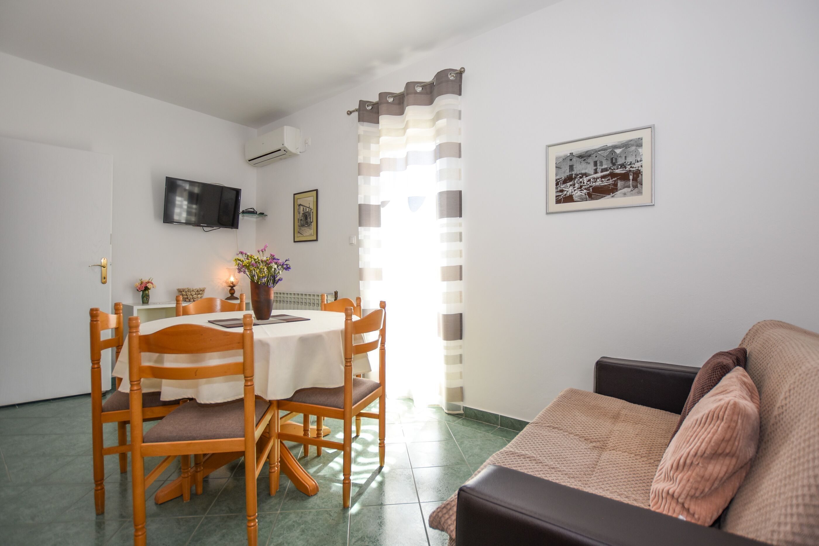 A dining area with a table and chairs, a television mounted on the wall, and a framed picture on the wall.