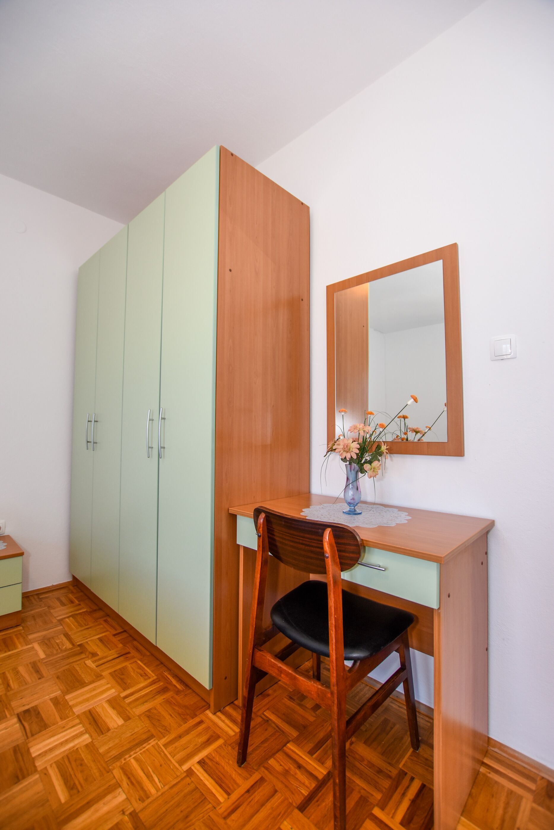 Ein Zimmer mit Schreibtisch, Stuhl, Spiegel und Kleiderschrank.
