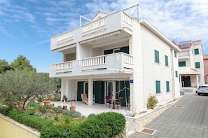A two-story building with balconies, a garden, and a car parked in front. - Apartments Dragica (Vodice)