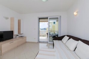 A modern living room with a flat-screen TV, a sofa, a sliding glass door leading to a balcony, and a small dining table. - Apartments Dragica (Vodice)