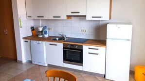A compact kitchen with white cabinets, a sink, a coffee maker, an oven, and a refrigerator. - Apartments Jure (Okrug Gornji)