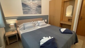 A neatly made bed with pillows, a bedside table with a lamp, a wardrobe, and a painting on the wall. - Apartments Jure (Okrug Gornji)