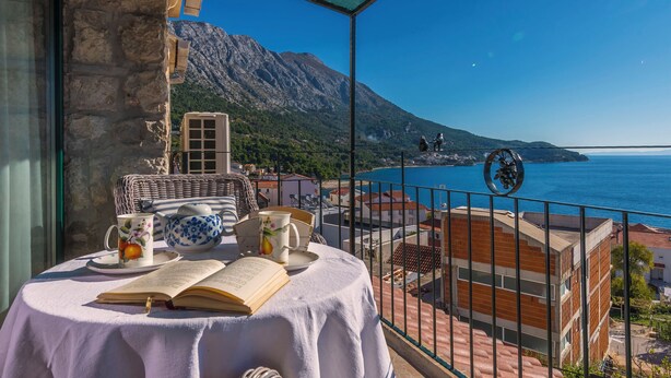 Un balcone con un tavolo apparecchiato per il tè, vista sulla costa e montagne sullo sfondo.