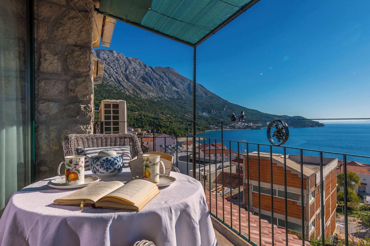 Un balcon avec une table dressée pour le thé, offrant une vue sur la côte et les montagnes en arrière-plan.