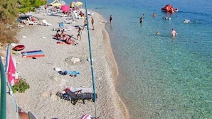 Una spiaggia con acque cristalline, lettini, ombrelloni e alcune persone che nuotano.
