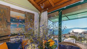 Una stanza con una grande finestra che si affaccia su un panorama suggestivo, un soffitto in legno e un tavolo con un bouquet di fiori.
