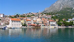 Un borgo costiero con edifici lungo la passeggiata, un cielo blu limpido e una montagna sullo sfondo.