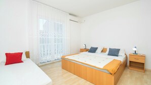 A bedroom with a large bed, a bedside table, a nightstand, and a window with sheer curtains. - Apartment Mijo (Vodice)